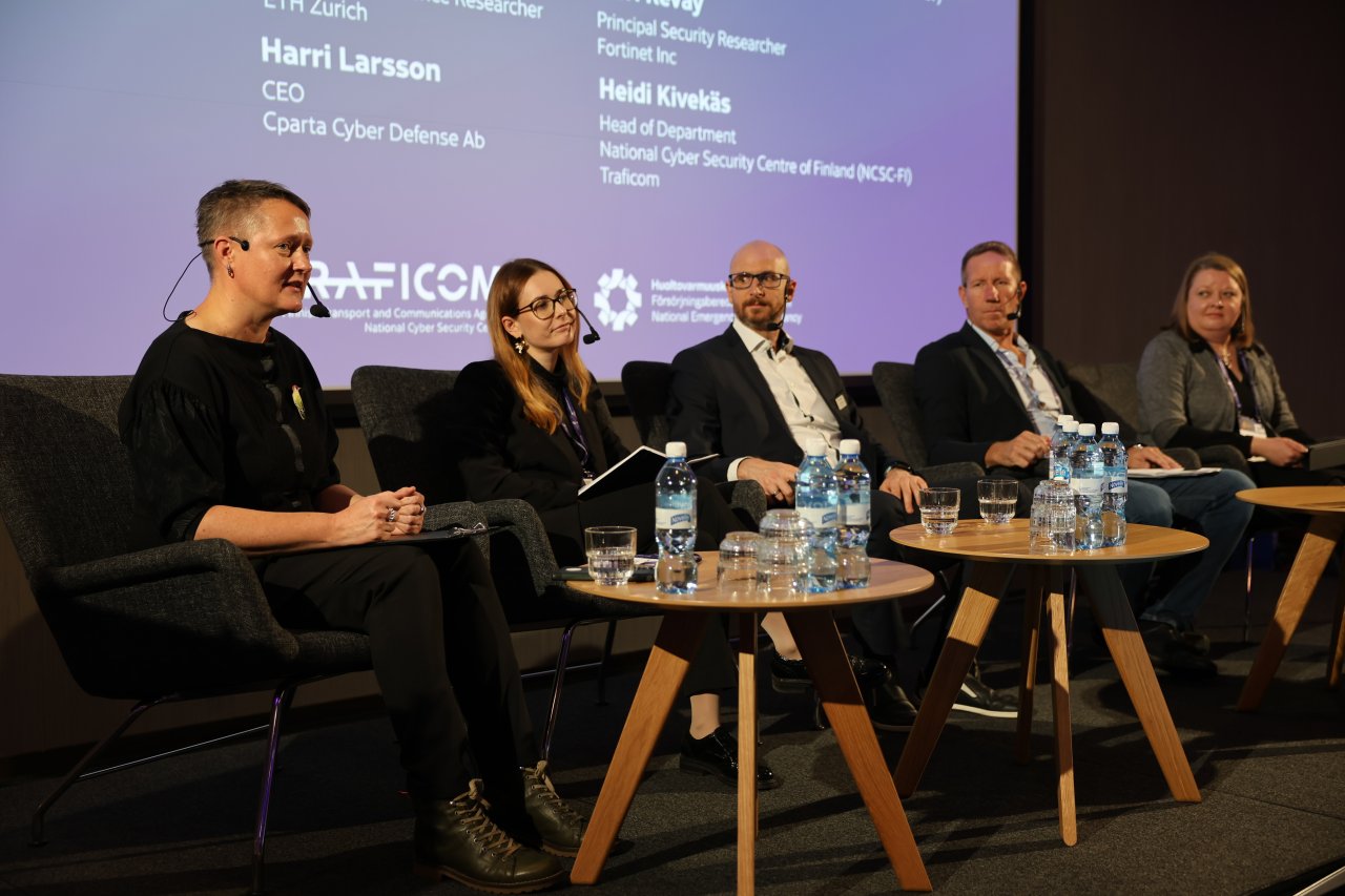 moderaattori ja viisi paneelikeskustelijaa seminaarin lavalla