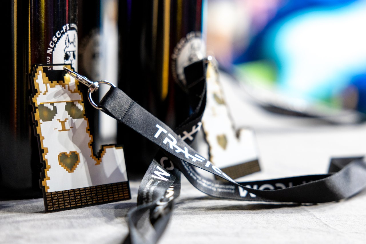 Kyberturvallisuuskeskuksen fanituotteita, kuten virtapiiripulmatehtävä-badge sekä juomapullo.