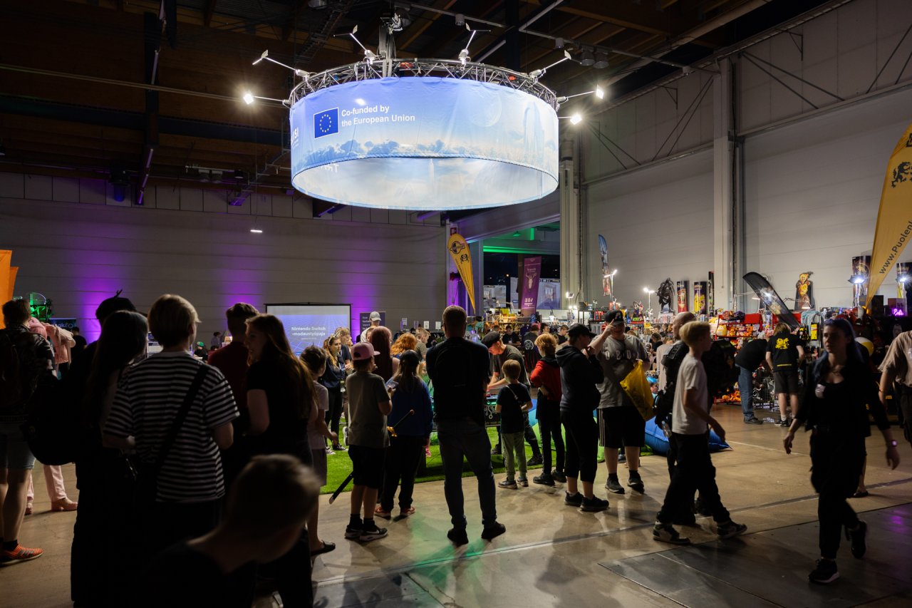 Traficomin Kyberturvallisuuskeskuksen ja Keskusrikospoliisin messuosasto. Väkijoukon yllä riippuu trussirakennelma, jossa on sinitaivaan ja futurististen pilvilinnojen kuvia.