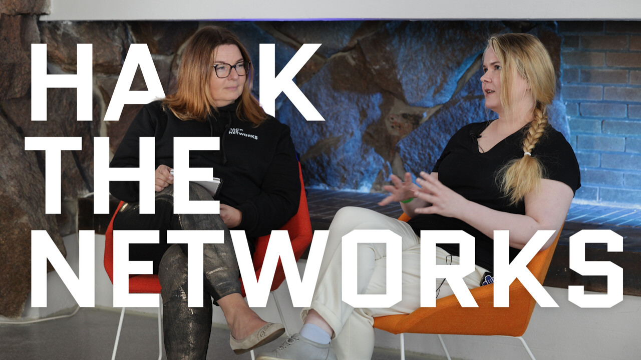 Teknologia- ja strategiajohtaja Kirsi Karlamaa haastattelemassa valkohattuhakkeri Mariana Leppäahoa, kumpikin istuu nojatuolissa takan edustalla. Hack the Networksin logo on editoitu ympäröimään heitä.