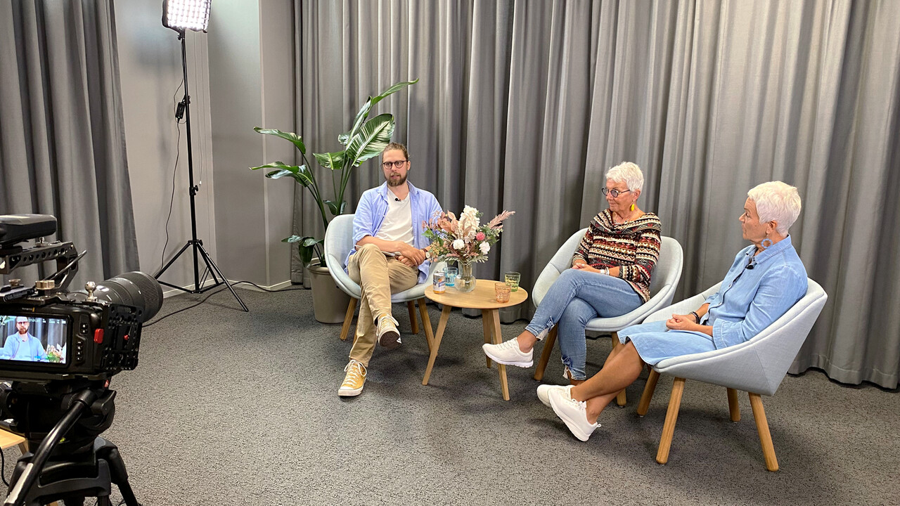 Tietoturva-asiantuntijamme Samuli Könönen keskustelee sarjassa turvallisesta netin käytöstä. Alt Text: Näkymä studion kulissien takaa sarjan kuvauksista. Kameran edessä tietoturva-asiantuntija Samuli Könönen ja kaksi senioria keskustelevat nojatuoleilla istuen.
